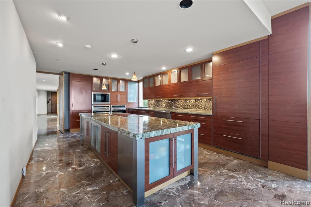 Kitchen with dark marble finish floors, dark stone countertops, an island with sink, modern cabinets, and recessed lighting