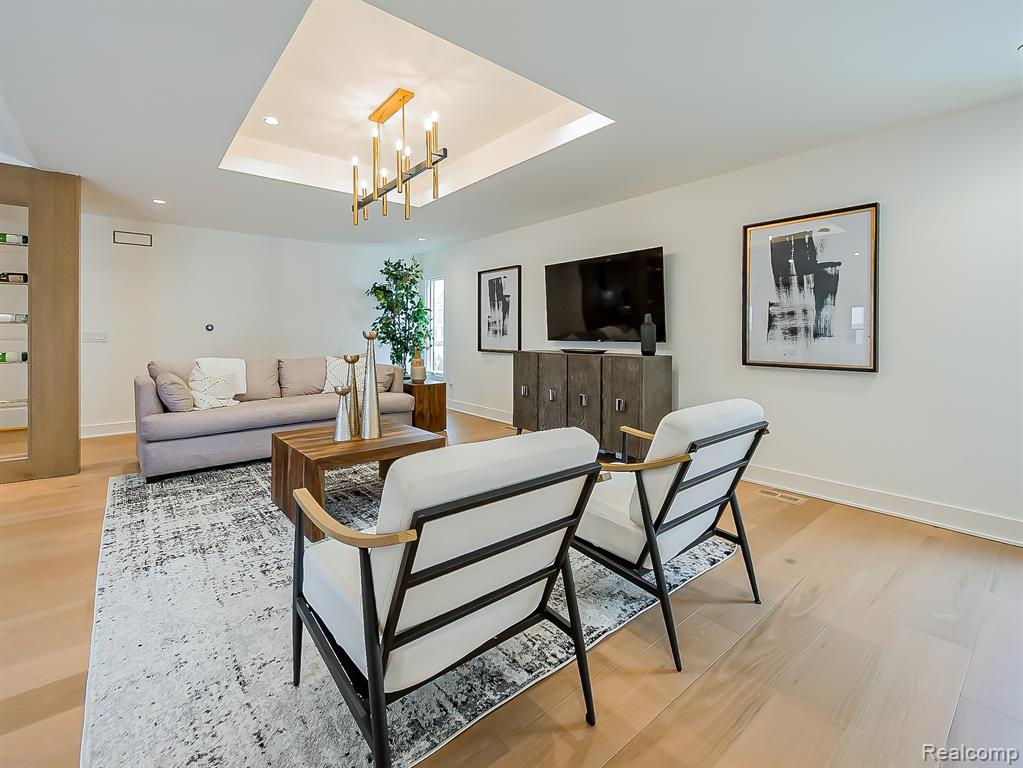 Living area with light wood-type flooring, a chandelier, a tray ceiling, and recessed lighting