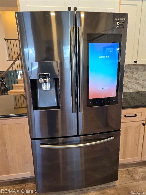 Kitchen view of stainless steel fridge, backsplash, and white cabinetry