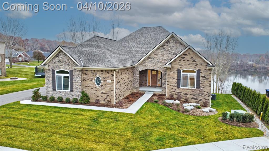 View of front of home with a front yard, brick siding, a shingled roof, and a water view