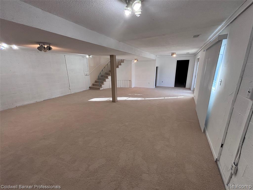 Finished below grade area with a textured ceiling, carpet flooring, and stairway