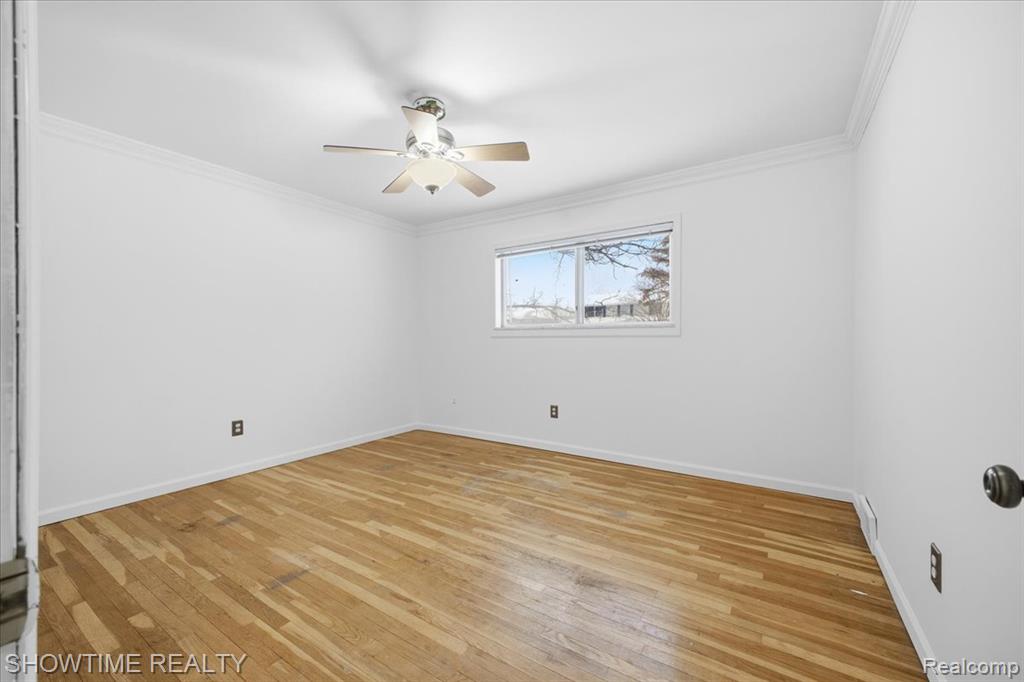 Spare room featuring ornamental molding, light wood-style flooring, and a ceiling fan