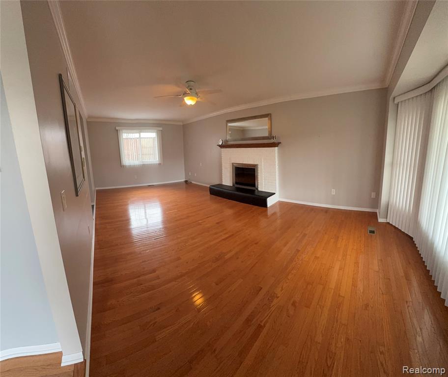 Unfurnished living room featuring light wood-style floors, a ceiling fan, ornamental molding, and a fireplace