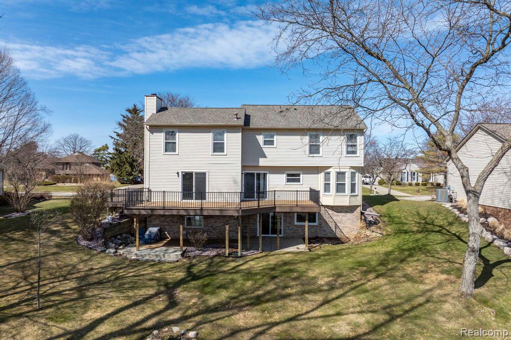 Back of property with a deck, a chimney, a patio, and a lawn