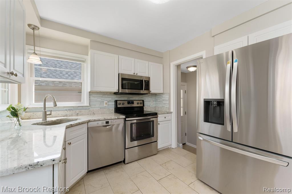 Kitchen with stainless steel appliances, light stone counters, and white cabinets
