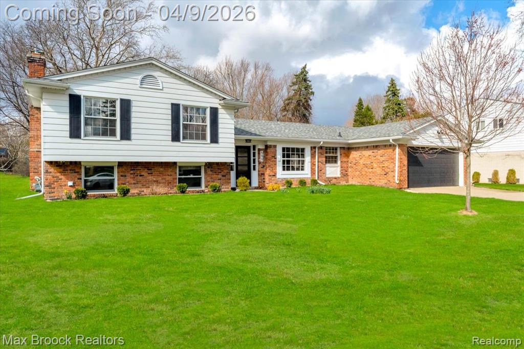 Tri-level home featuring an attached garage, a chimney, brick siding, and a front lawn