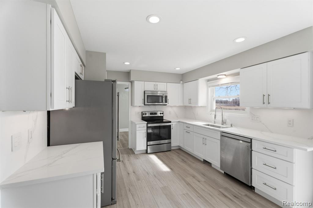 Kitchen featuring white cabinetry, stainless steel appliances, light wood-type flooring, light stone counters, and recessed lighting