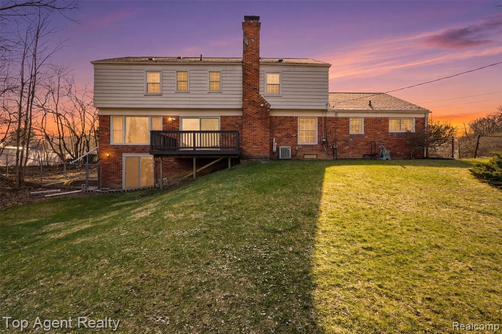 Back of property featuring brick siding, a lawn, a chimney, and a wooden deck