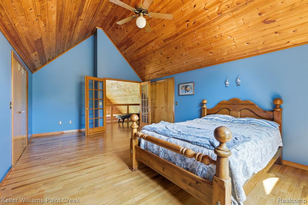 Vaulted wood-paneled ceiling with ceiling fan, wood-finish flooring, two sets of French doors, and a solid wood door