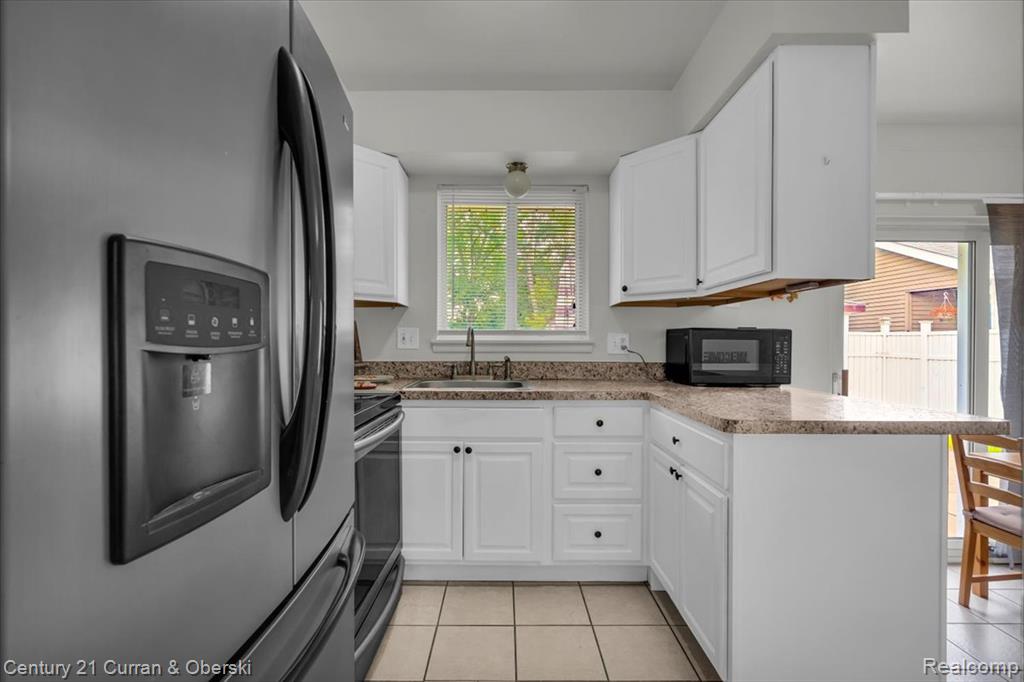 Kitchen featuring stainless steel appliances, light tile patterned flooring, white cabinets, a peninsula, and light countertops