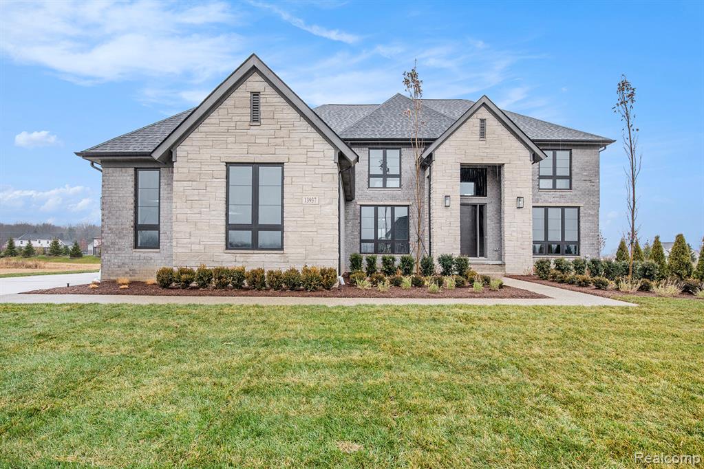 French country home featuring a front lawn, stone siding, roof with shingles, and brick siding
