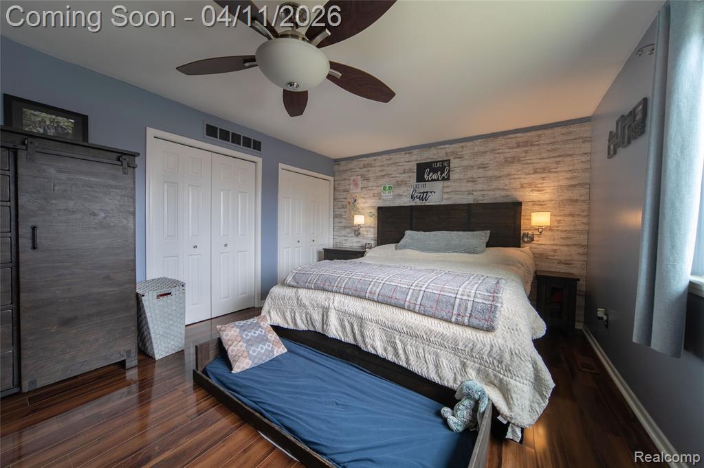 Bedroom featuring an accent wall, multiple closets, dark wood-type flooring, and a ceiling fan