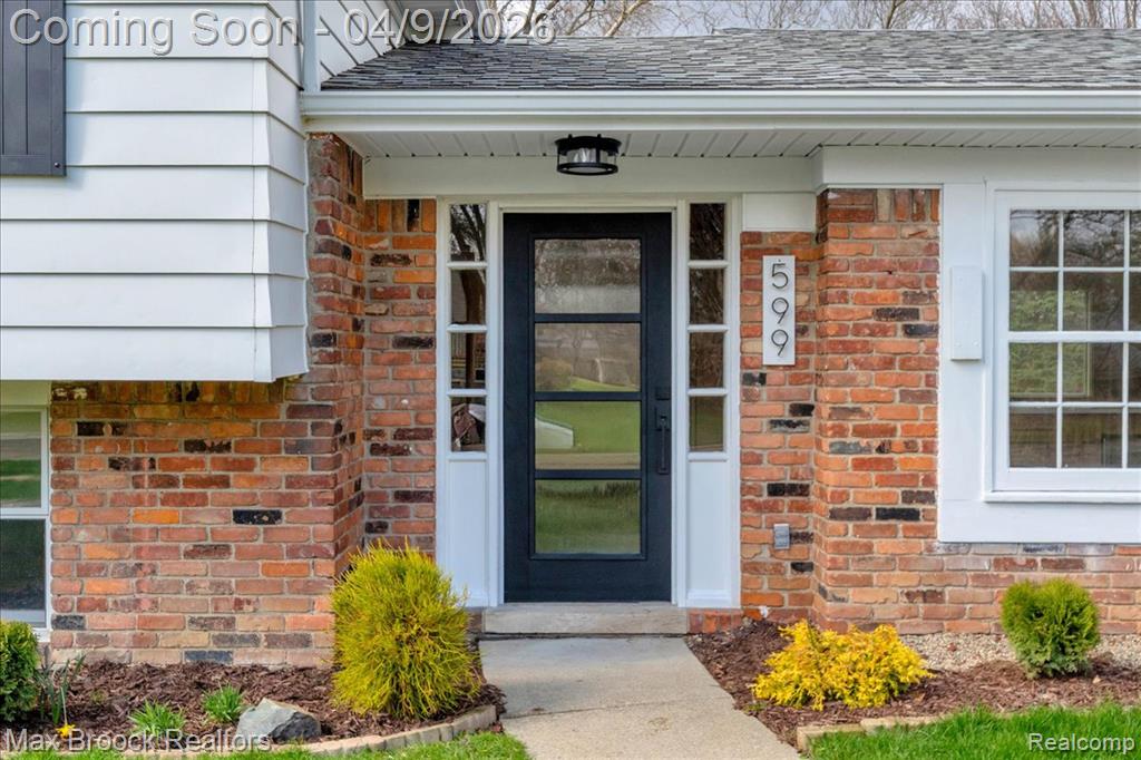 View of exterior entry featuring brick siding and a shingled roof