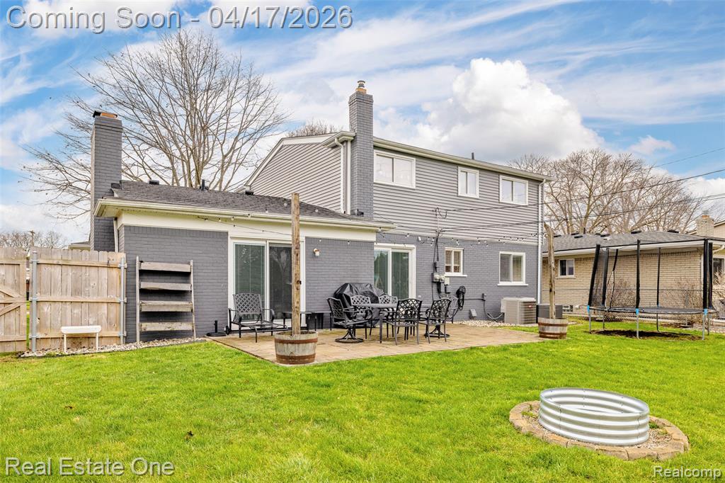Rear view of house featuring a trampoline, a chimney, a patio area, brick siding, and a fenced backyard