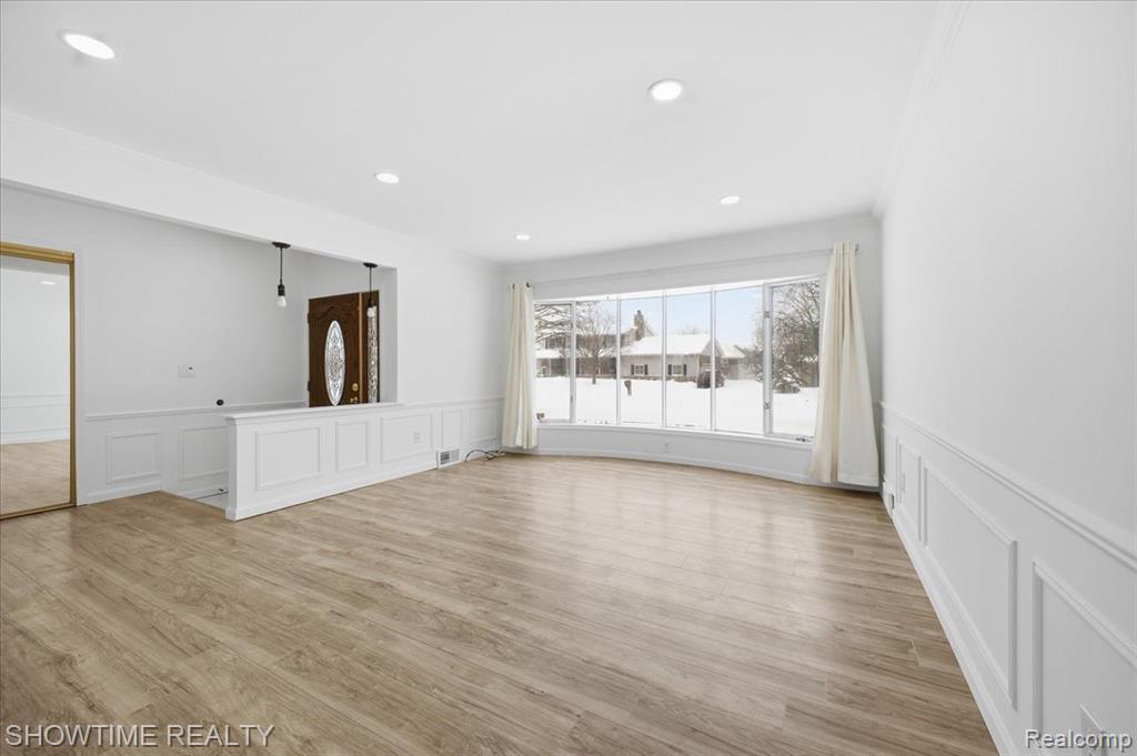 Empty room featuring a decorative wall, wainscoting, light wood-style flooring, and recessed lighting