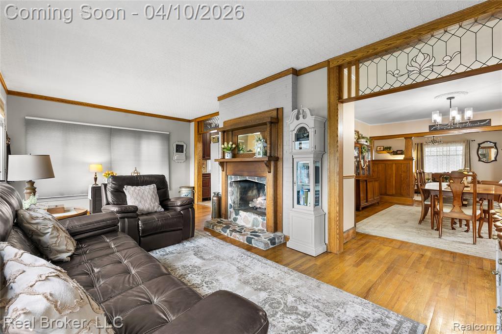 Living room featuring hardwood / wood-style floors, a stone fireplace, crown molding, and a chandelier