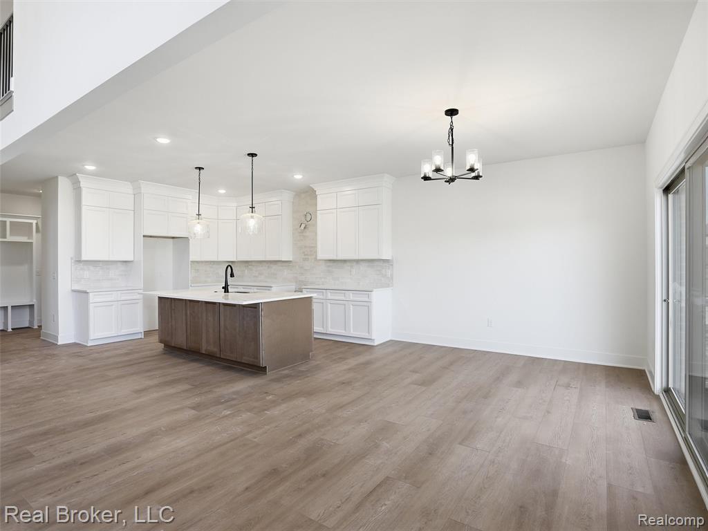 Kitchen featuring two tone cabinetry, a kitchen island with sink, open floor plan, hanging lights, and dark wood-style flooring