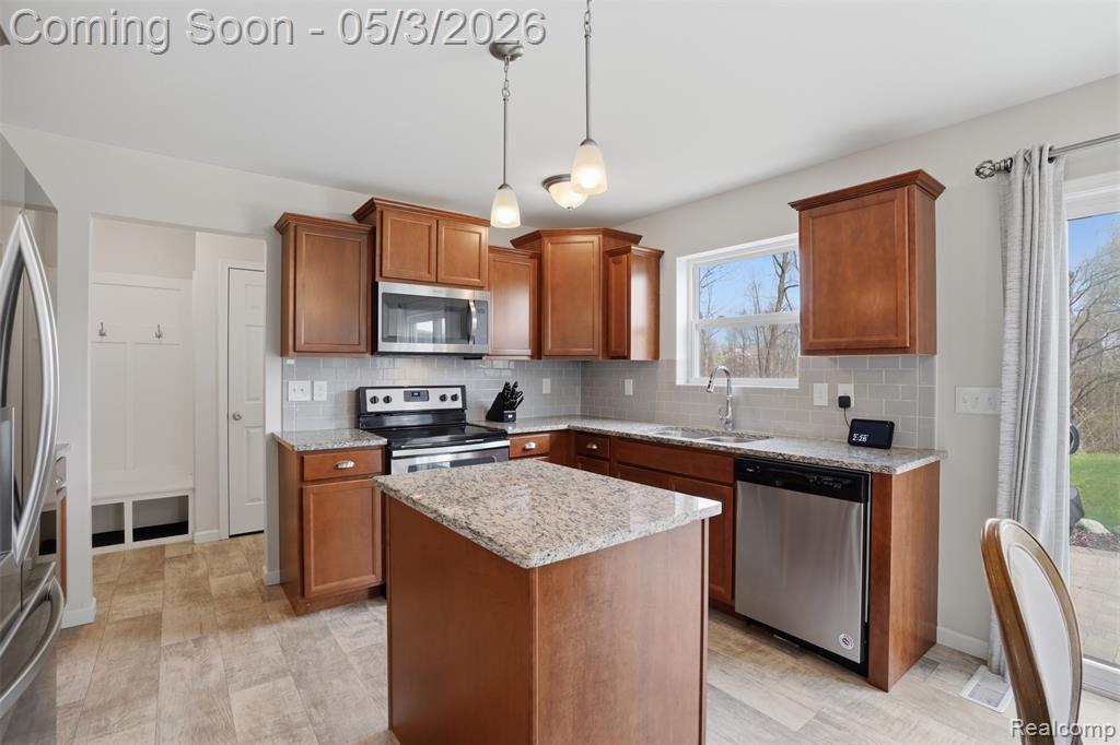 Kitchen featuring wood finish cabinets, light stone countertops, stainless steel appliances, a center island, and hanging light fixtures