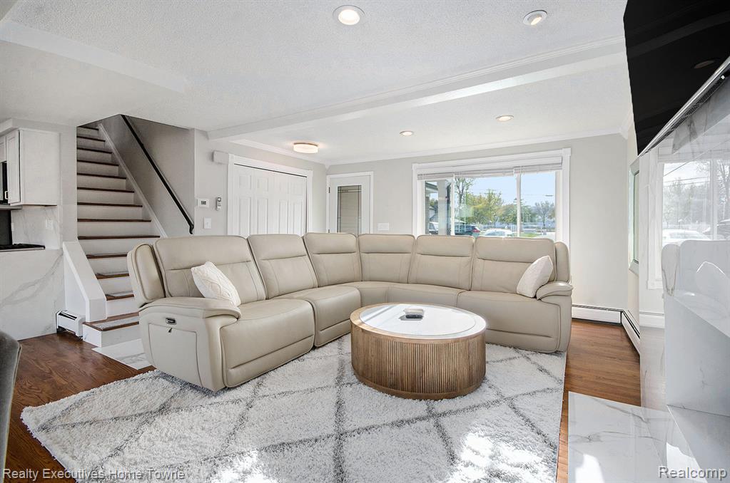 Living room featuring baseboard heating, a textured ceiling, crown molding, wood finished floors, and recessed lighting