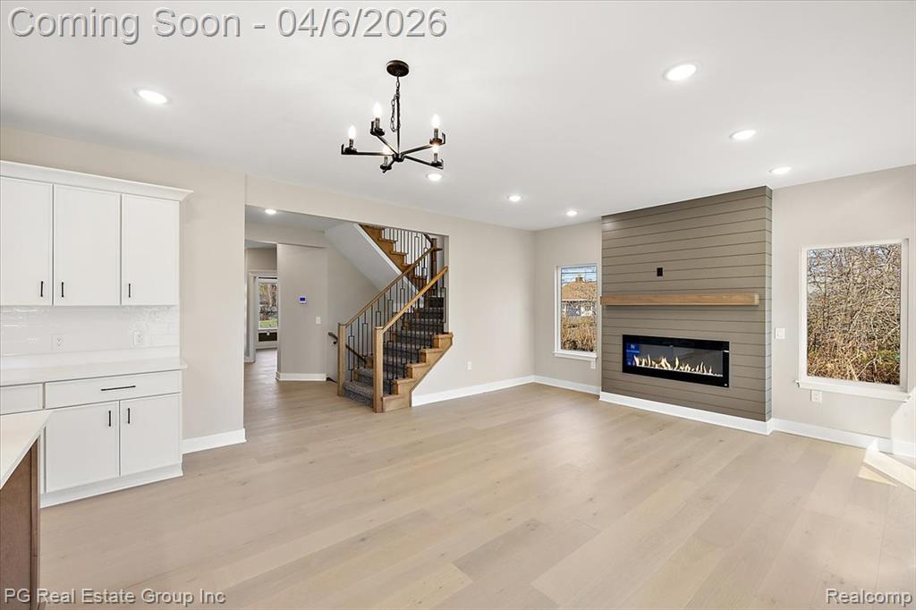 Unfurnished living room with a large fireplace, light wood finished floors, and suspended lighting