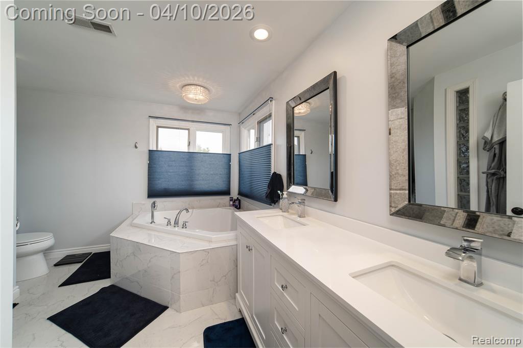 Full bath featuring double vanity, a garden tub, light marble finish floors, and recessed lighting