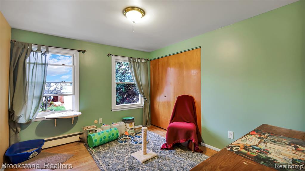 Bedroom with a baseboard heating unit, light wood-style floors, and a closet