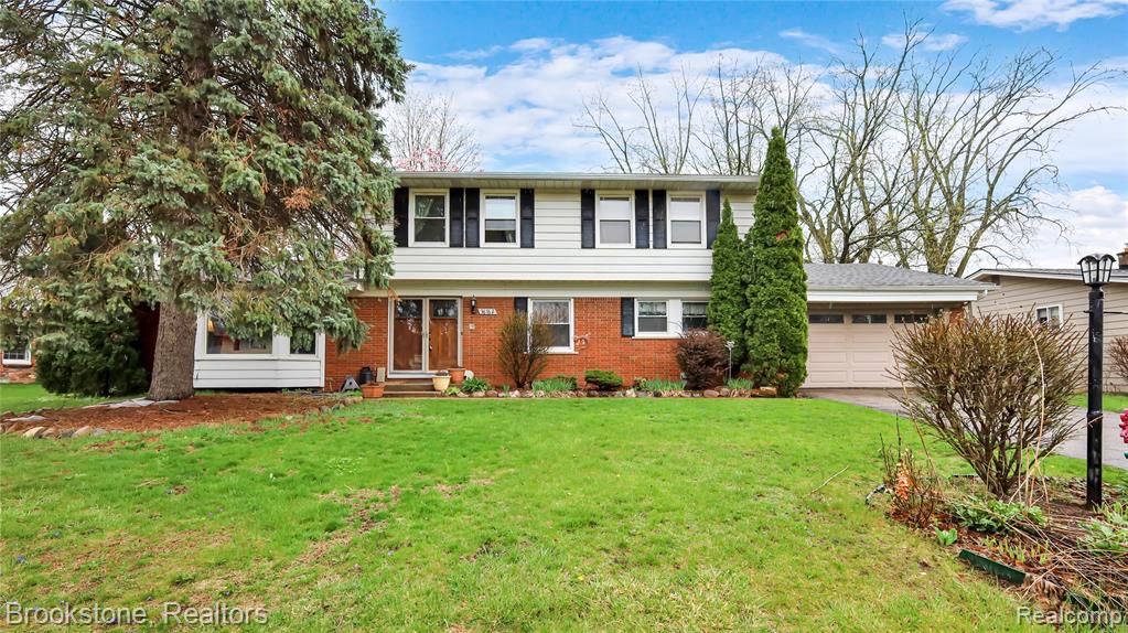 Colonial house with a front yard, brick siding, an attached garage, entry steps, and driveway