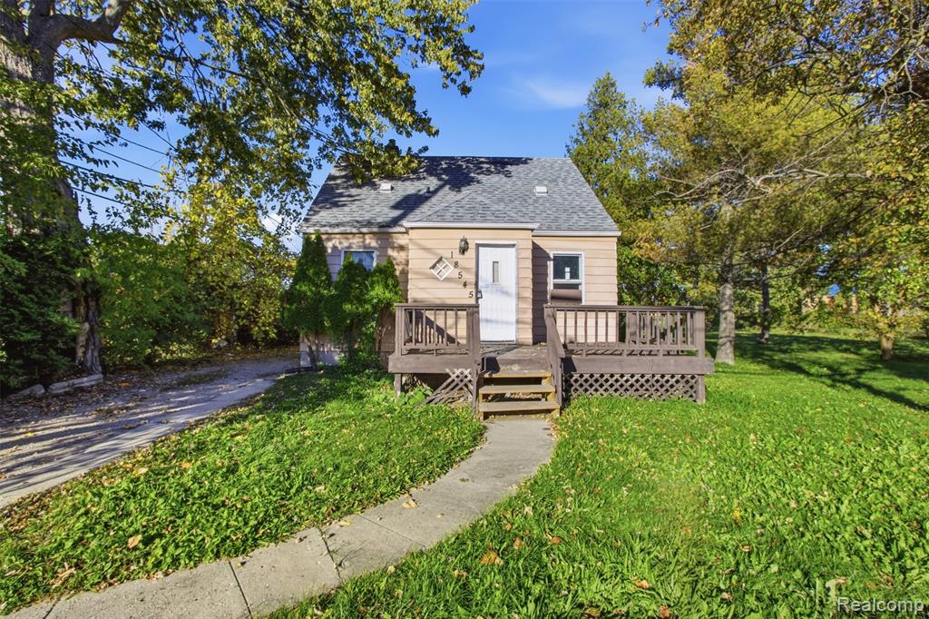 Single-story exterior featuring light-toned horizontal siding, a pitched shingle roof, a front wooden deck with lattice skirting, and a concrete walkway