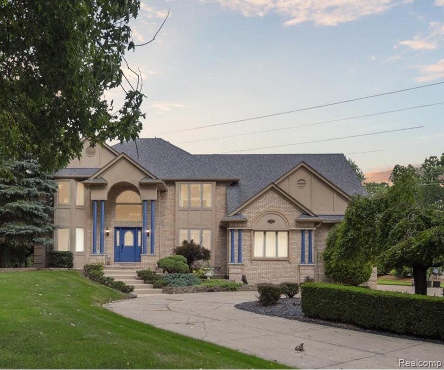 Brick facade residence featuring a prominent arched entry, dual blue entry doors, a multi-tiered concrete driveway, and established landscaping