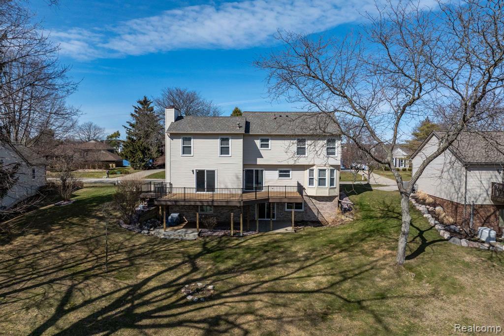 Rear view of property featuring a wooden deck, a chimney, and a lawn