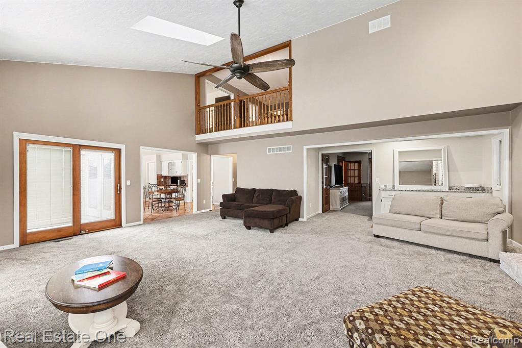 Carpeted living area featuring a skylight, high vaulted ceiling, ceiling fan, and a textured ceiling