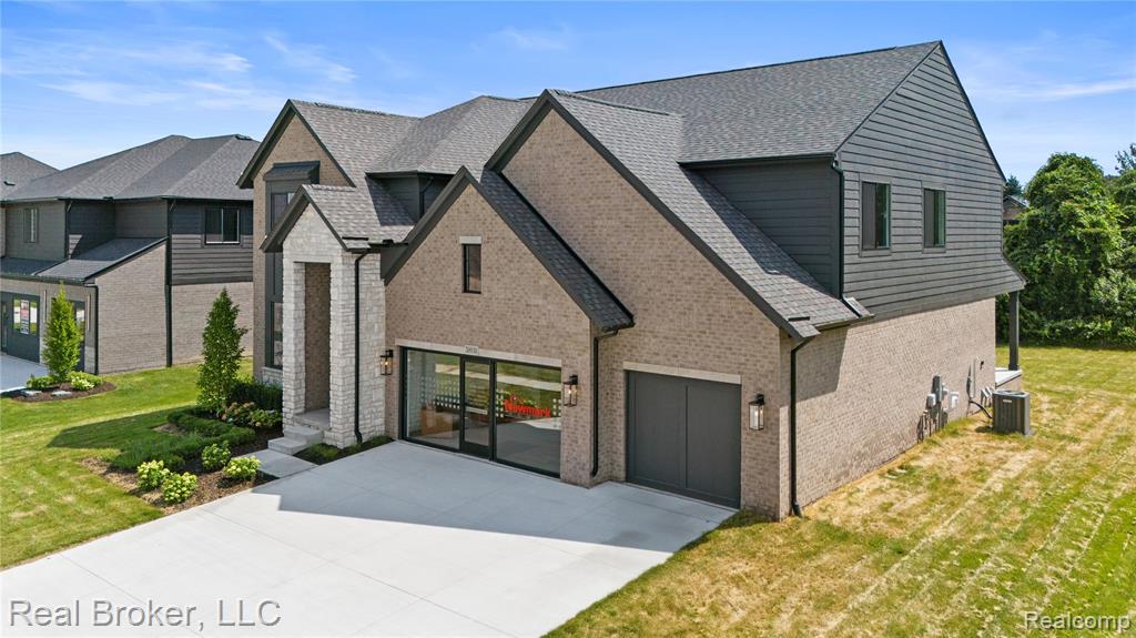 French country home with a front yard, concrete driveway, brick siding, and a shingled roof