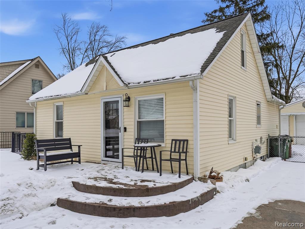 Snow covered back of property featuring a wooden deck, a gate, and a garage