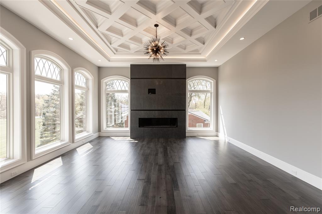 Unfurnished living room with a large fireplace, coffered ceiling, dark wood-style floors, recessed lighting, and ornamental molding