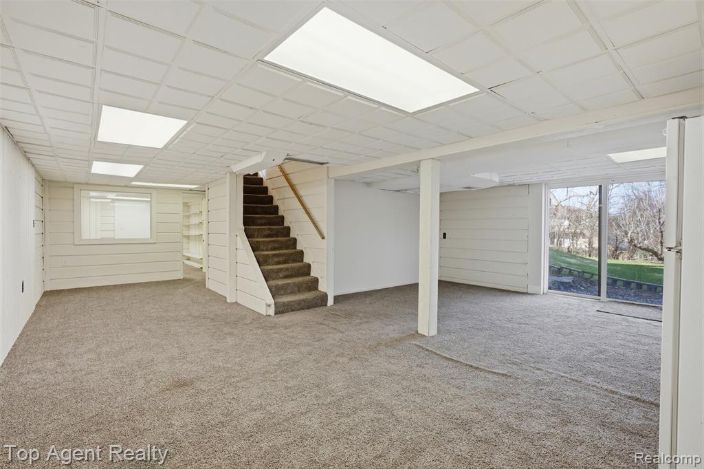 Basement featuring freestanding refrigerator, light carpet, and wood walls
