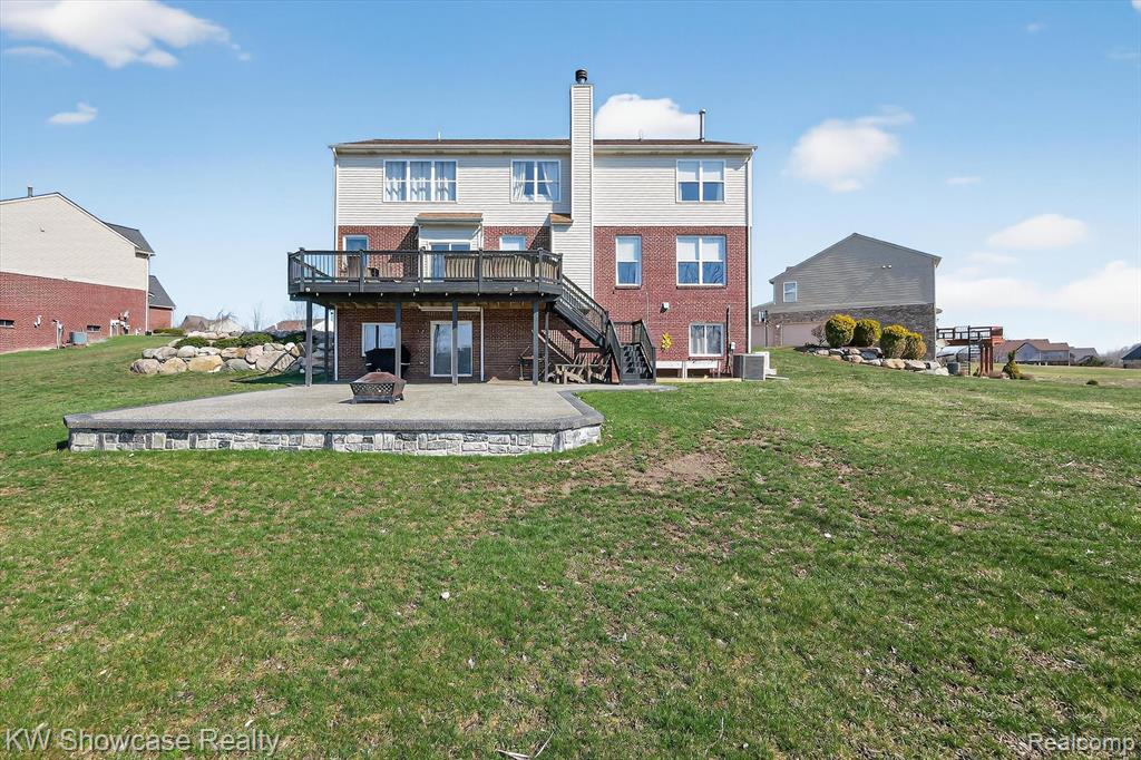 Rear view of property with a deck, an outdoor fire pit, a patio area, a lawn, and brick siding