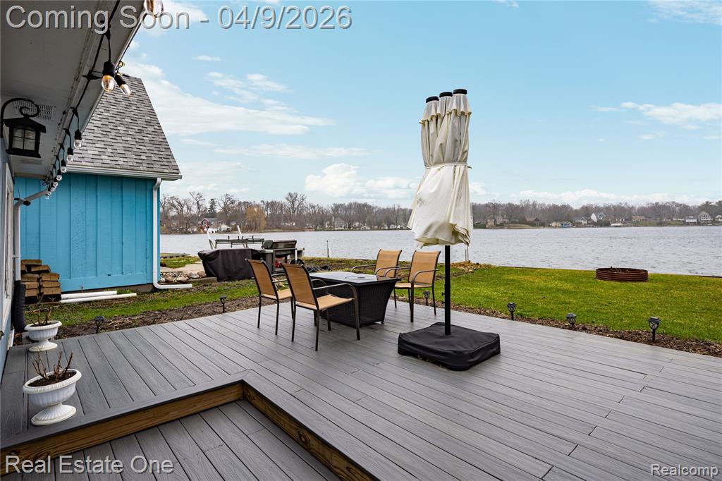 Wooden terrace featuring a water view and a lawn