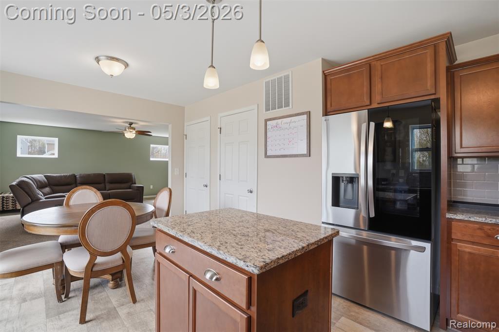 Kitchen with stainless steel fridge with ice dispenser, a center island, hanging light fixtures, open floor plan, and light stone countertops
