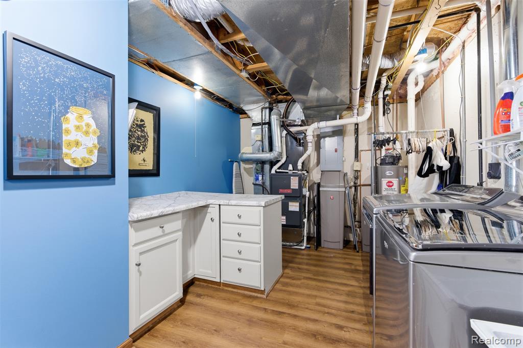 Unfinished below grade area with light wood-type flooring, washer and dryer, electric panel, and water heater