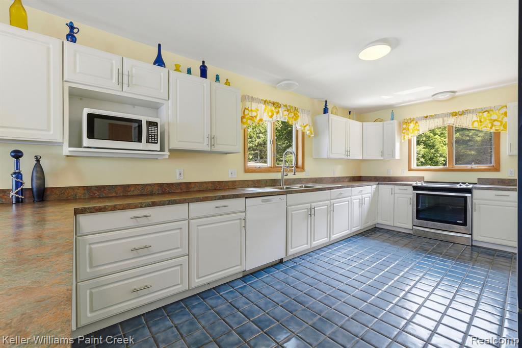 Spacious kitchen featuring extensive white cabinetry, durable countertops, stainless steel appliances, a built-in microwave, and tiled flooring