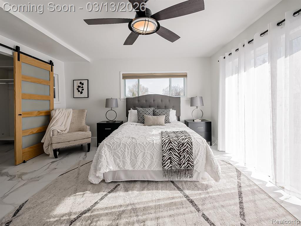 Bedroom featuring a barn door, multiple windows, a ceiling fan, and marble look tile flooring