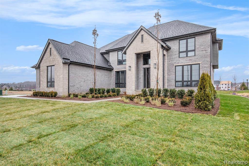 French country style house with brick siding, a front yard, and roof with shingles