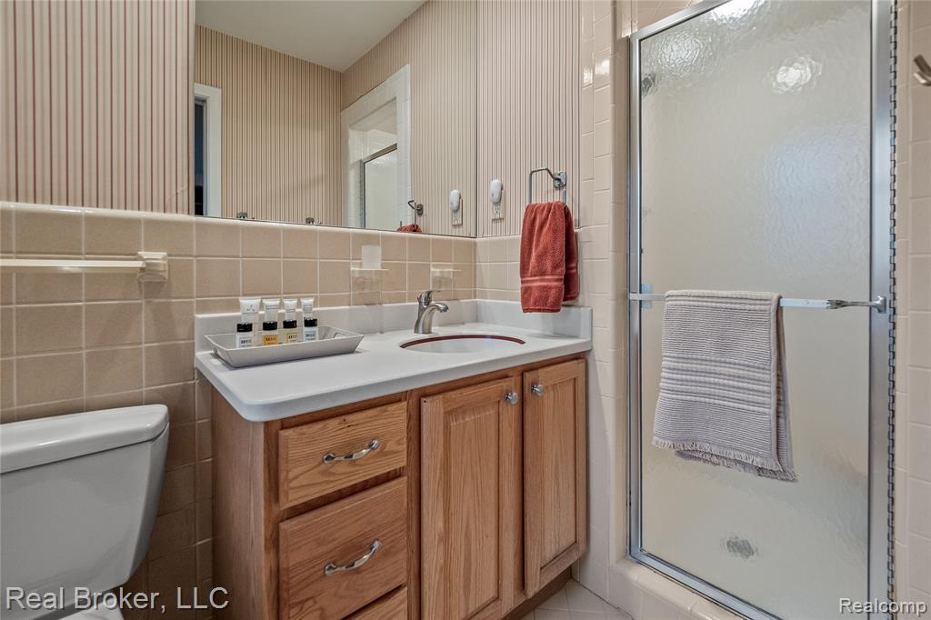 Bathroom with vanity, a stall shower, tile walls, backsplash, and wallpapered walls