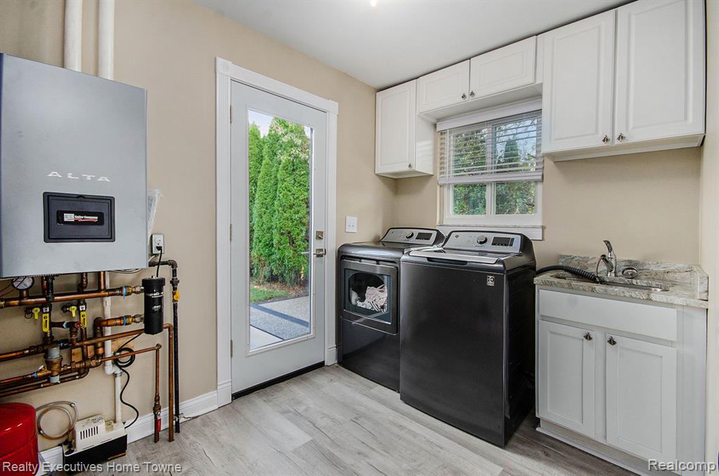 Laundry room with water heater, light wood-type flooring, washing machine and clothes dryer, and cabinet space