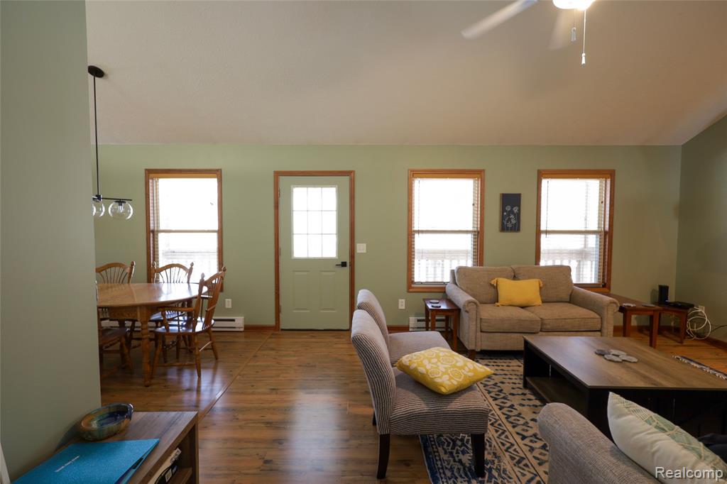 Living room featuring dark wood-style floors, a ceiling fan, and a baseboard heating unit