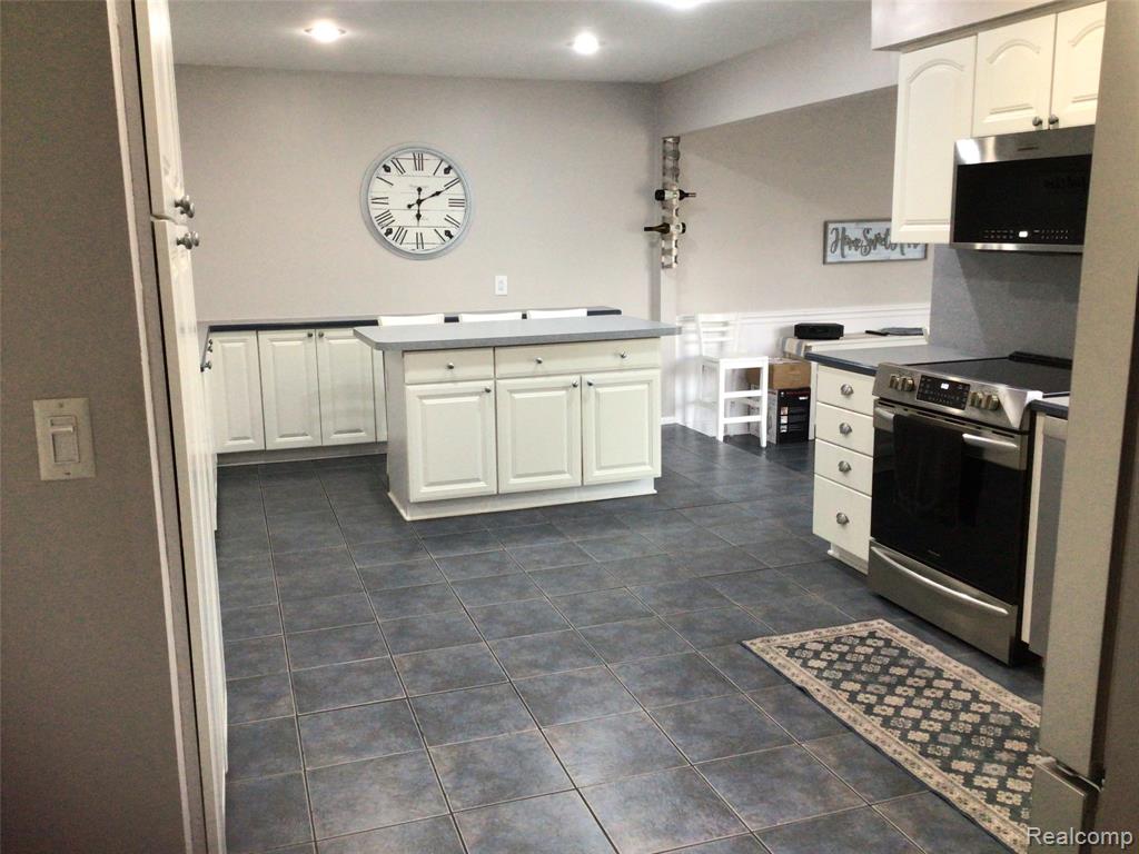 Kitchen with white cabinetry, stainless steel appliances, a kitchen island, recessed lighting, and dark tile patterned flooring