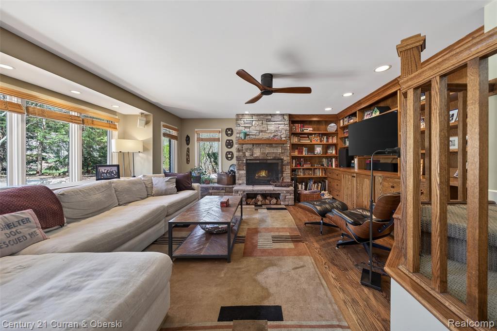 Living area with recessed lighting, wood finished floors, a stone fireplace, ceiling fan, and built in shelves