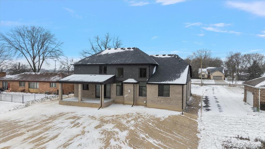 Snow covered property with brick siding and a patio