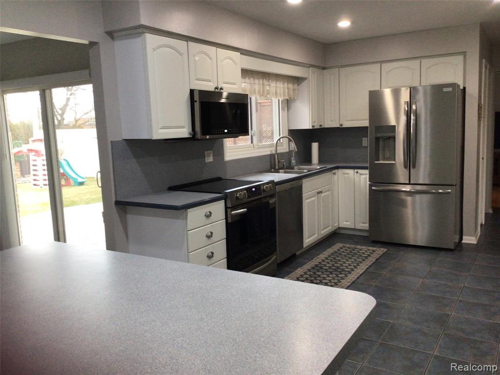 Kitchen with stainless steel appliances, white cabinets, recessed lighting, dark countertops, and dark tile patterned floors