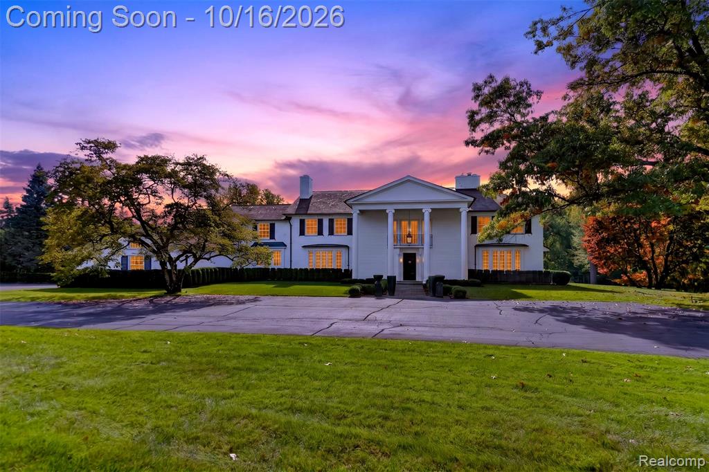 Classical Colonial exterior featuring a prominent two-story portico, multi-pane windows, dual chimneys, and an expansive front lawn